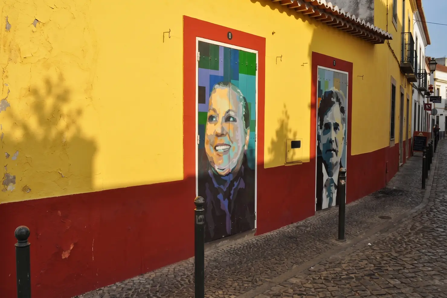 Rua de Santa Maria, in the Zona Velha. Around 200 doors have been painted since 2011, and the walk ends at the ochre walls of the São Tiago fortress.