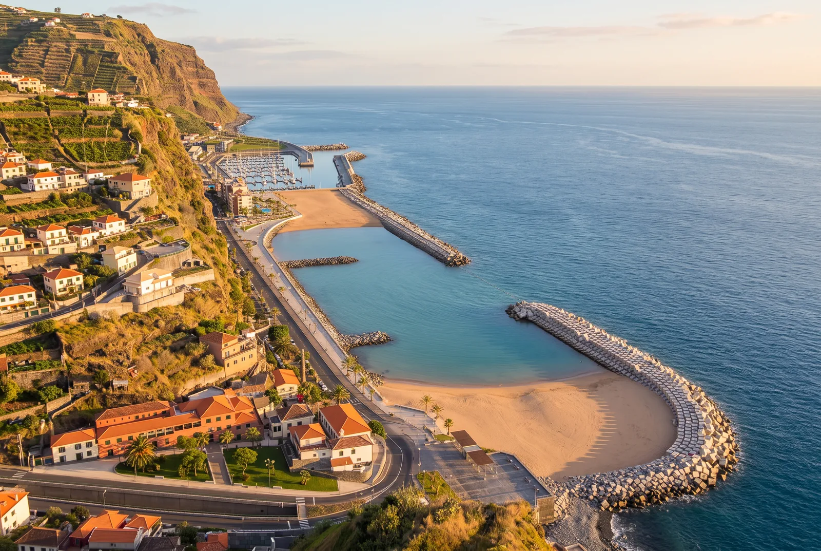 A golden sand beach held between two breakwaters beside the marina at Calheta, at golden hour