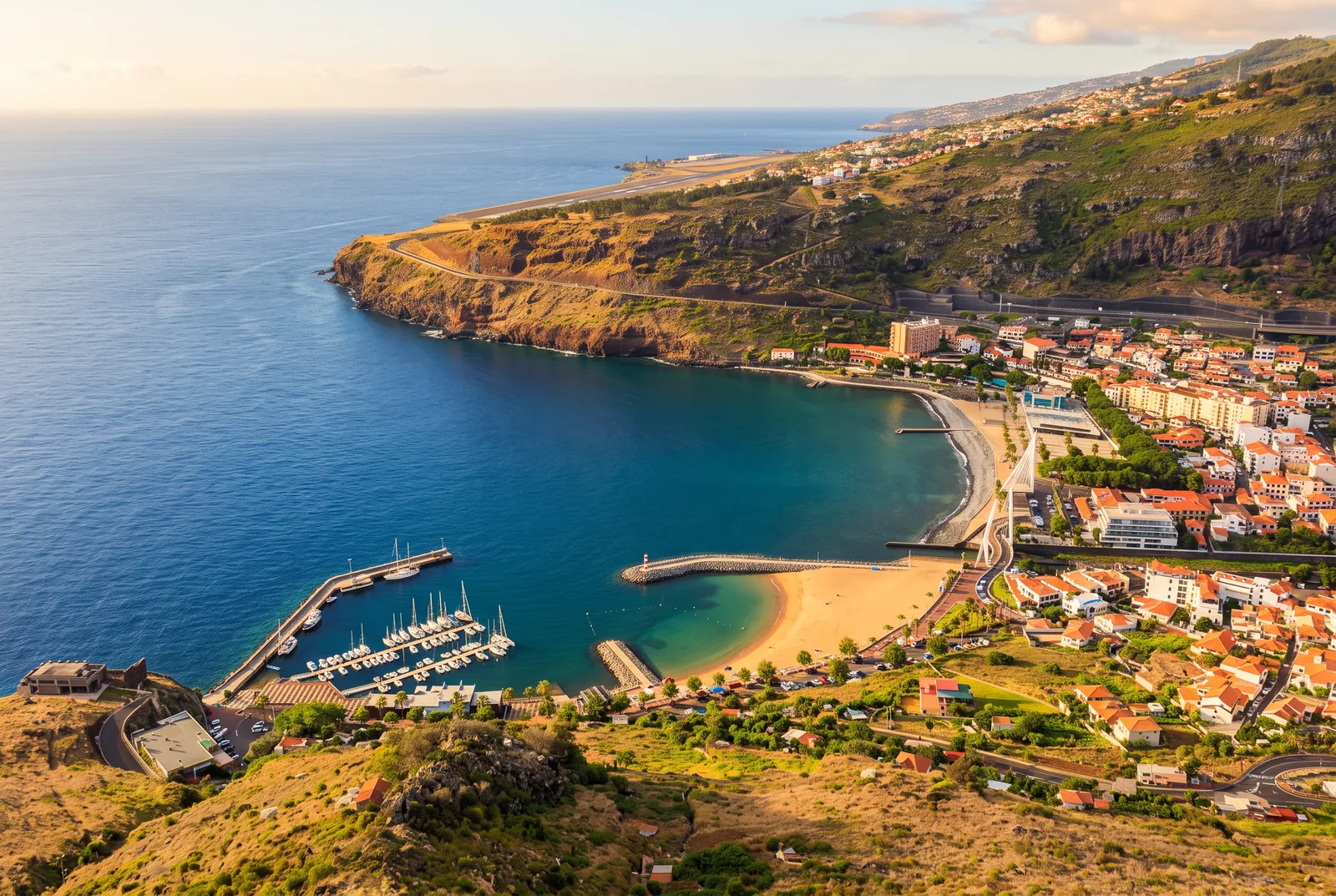 Machico bay with its marina, golden beach and the airport runway on the headland beyond