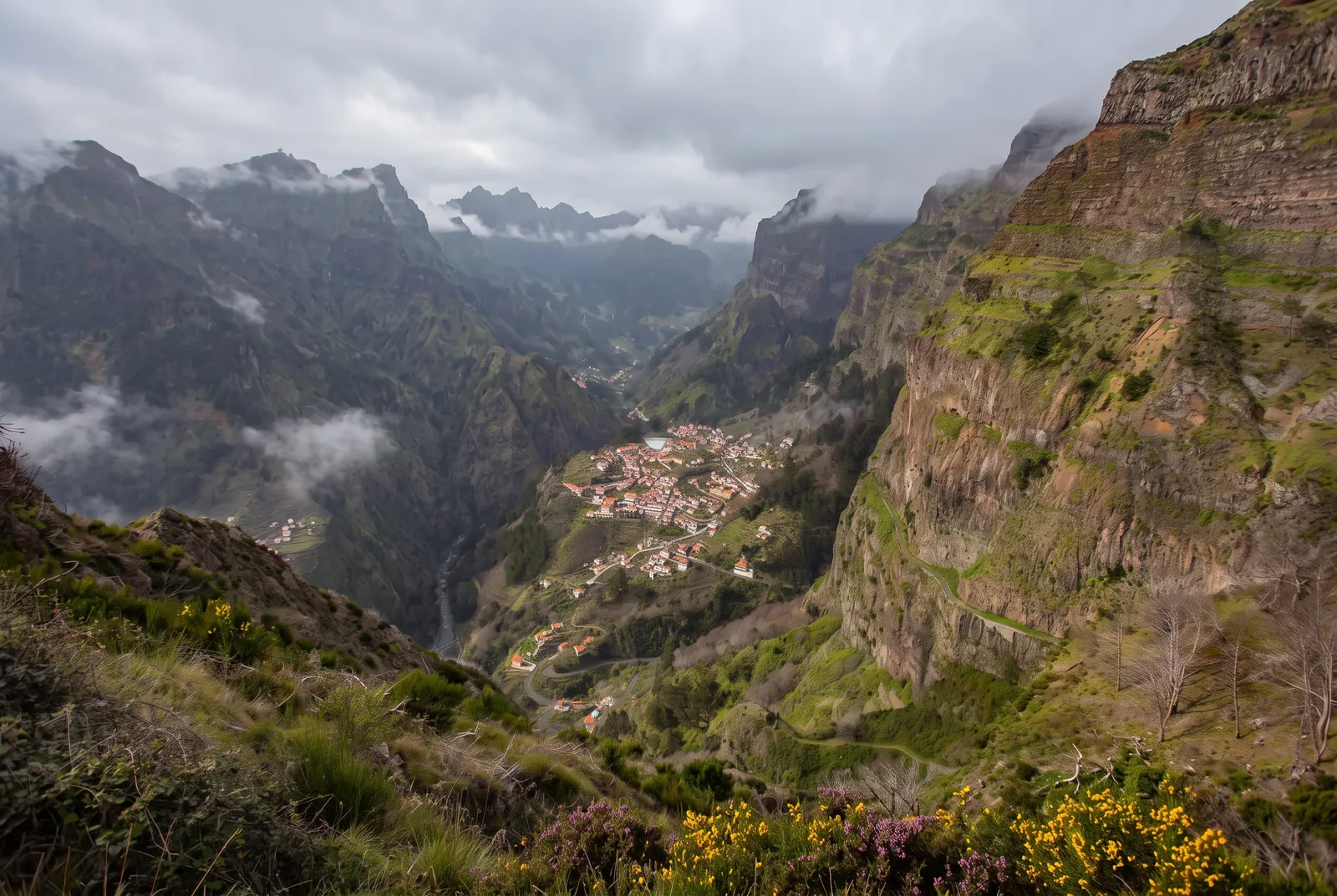 The Curral das Freiras valley under a flat overcast winter sky, with mist clinging to the ridges