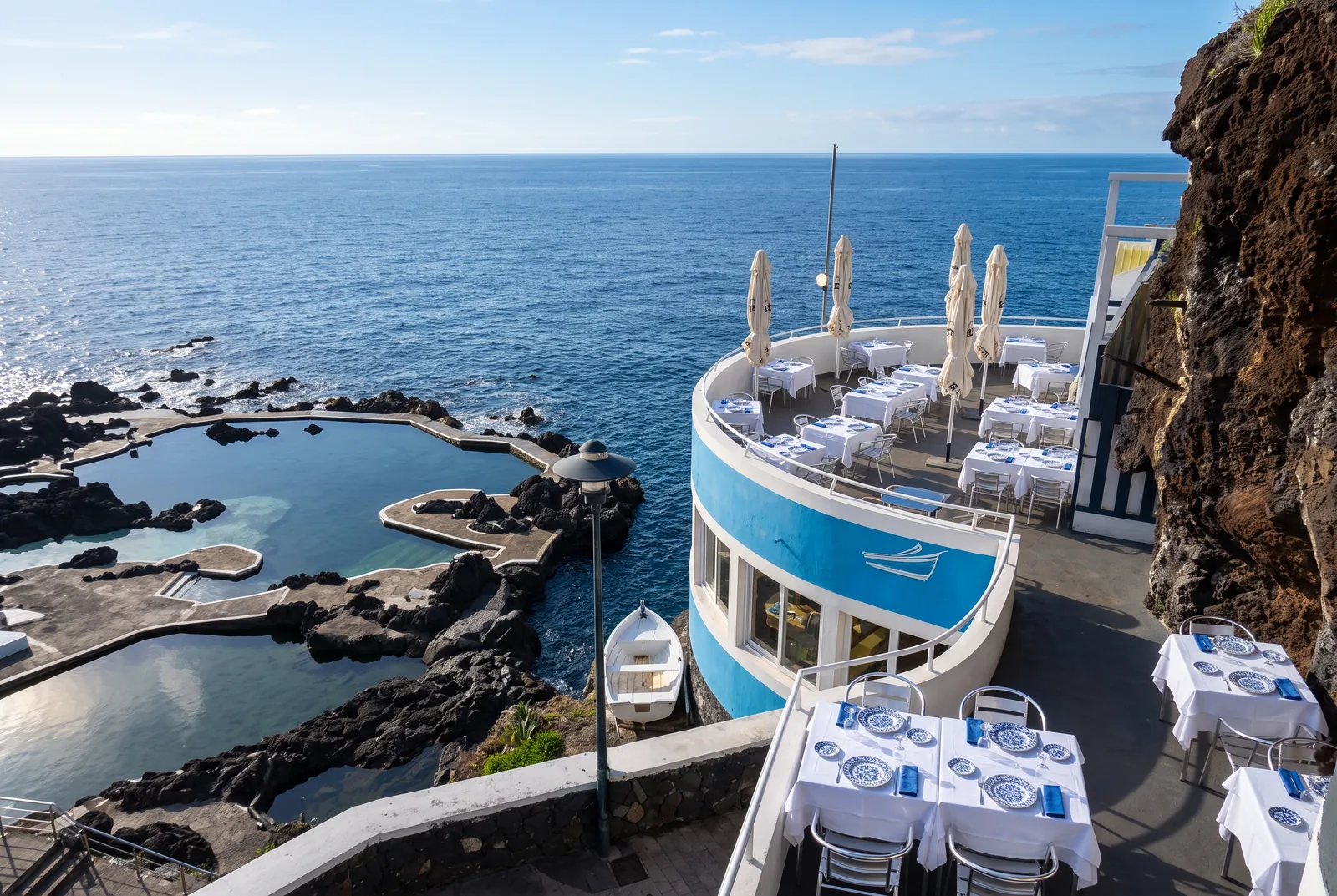 A rooftop restaurant terrace with laid tables above lava pools and the Atlantic