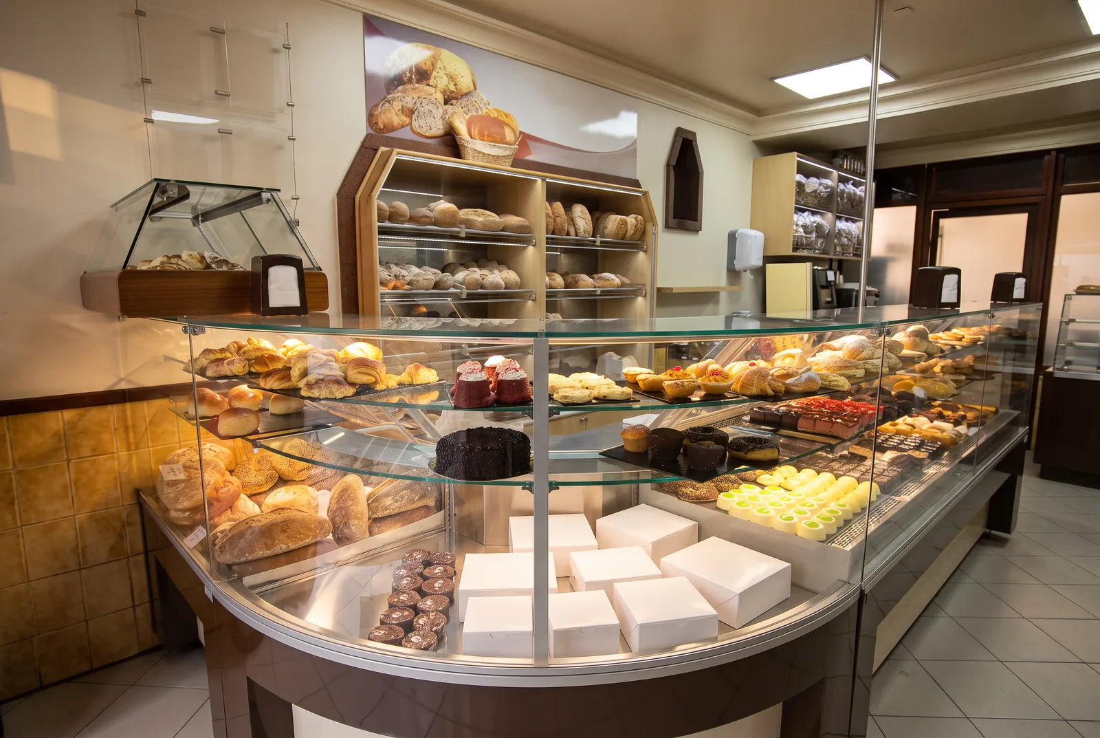 The curved display counter of a neighbourhood bakery, with breads, pastries and cake boxes