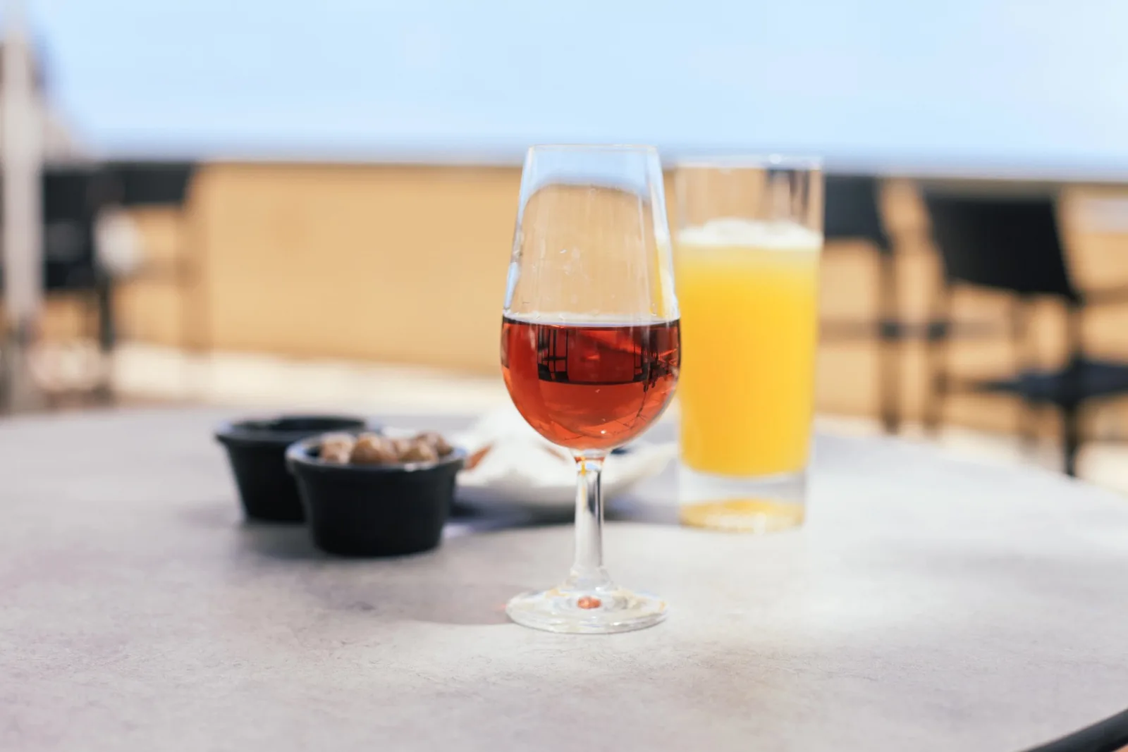 Two chilled island drinks on a sunlit table, one amber and one pale, with a small dish of olives