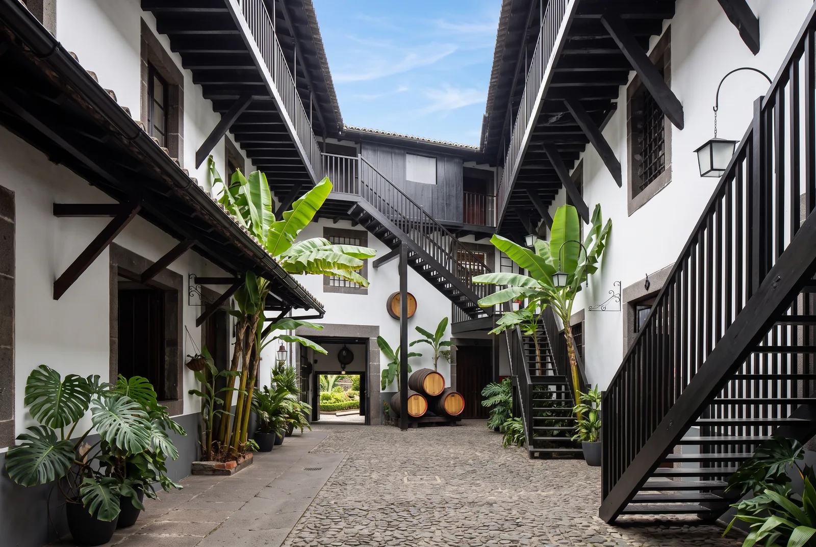 The cobbled courtyard of a Madeira wine lodge, with dark timber galleries, banana plants and stacked casks