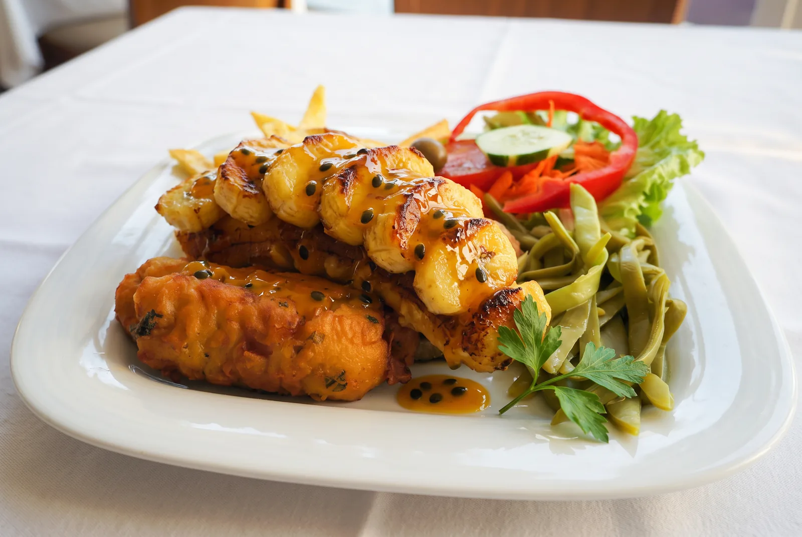 A plate of battered black scabbard fish topped with sautéed banana and passion fruit sauce