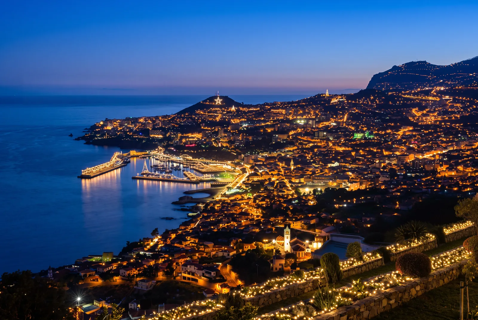 Funchal at blue hour with the Christmas lights on, the harbour breakwater below and the city climbing the hillside
