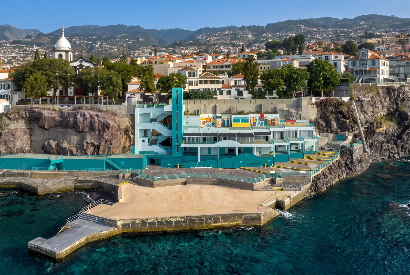 The Barreirinha bathing complex in Funchal's old town on a clear winter day, with the church of Santa Maria Maior above the cliff