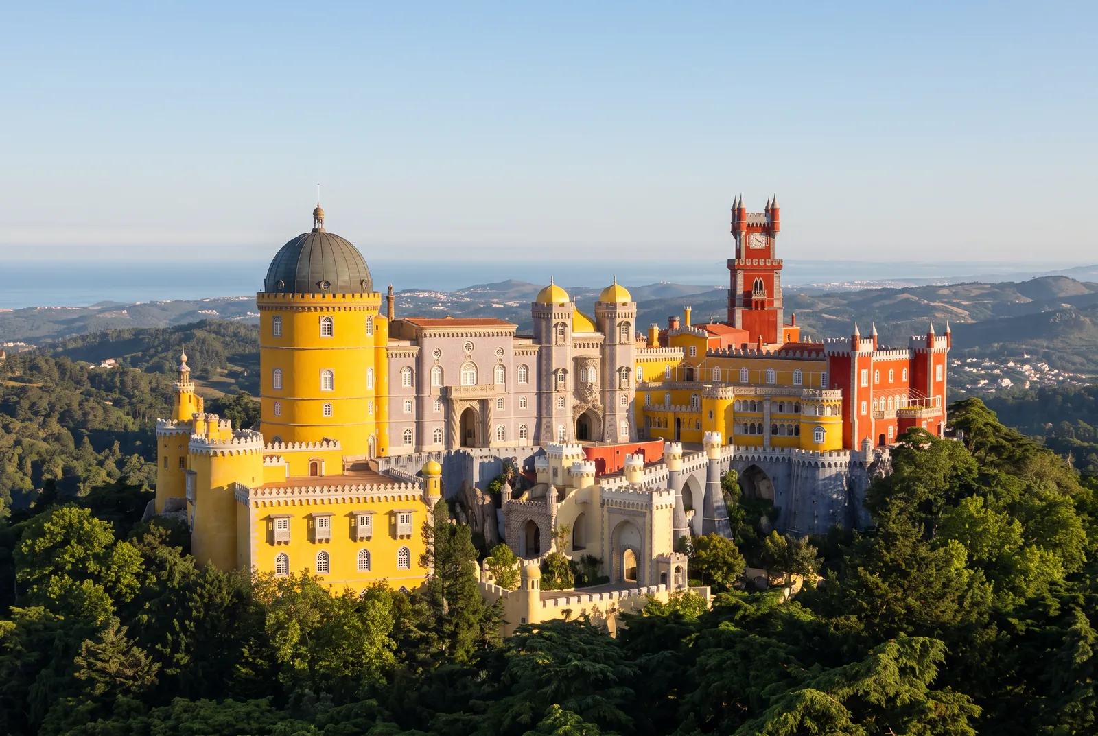 The Pena Palace on the summit of the Serra de Sintra in early morning light, its yellow, red and lilac blocks above the forest