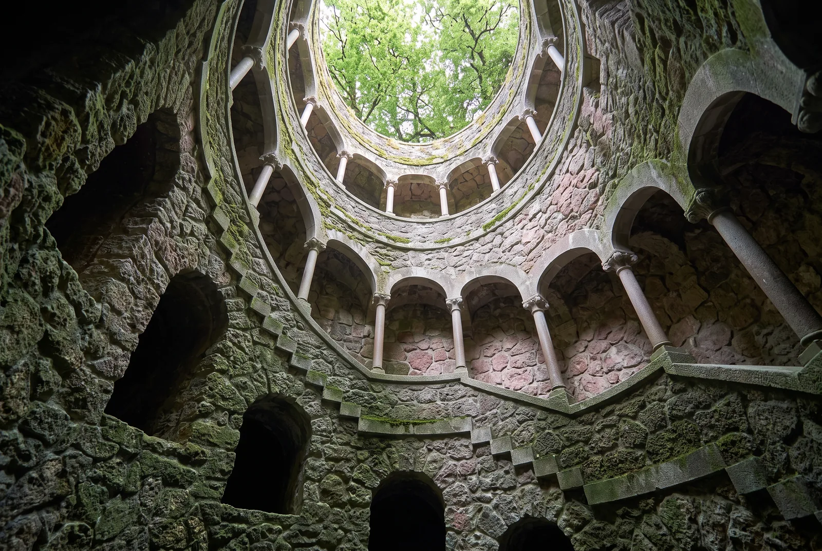 The Initiation Well at Quinta da Regaleira seen from a landing, its spiral stair and arcades rising to the opening above