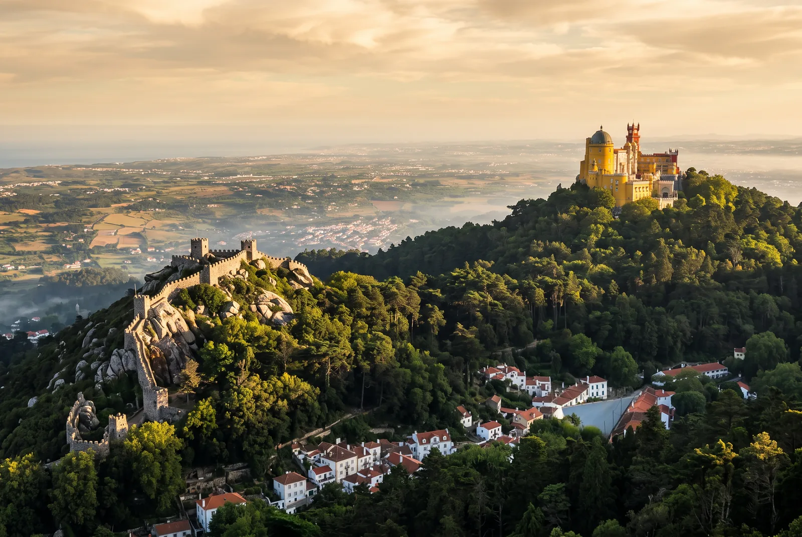 The Serra de Sintra ridge at golden hour, with the Moorish Castle walls on a lower crest and Pena Palace on the summit beyond