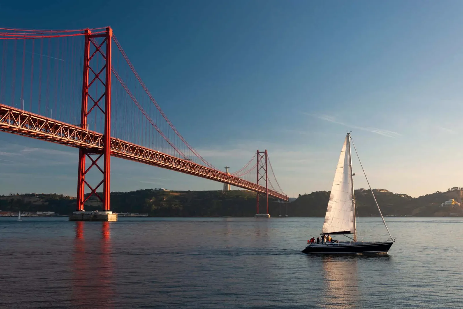The red 25 de Abril bridge over the Tagus with a sailing boat passing beneath
