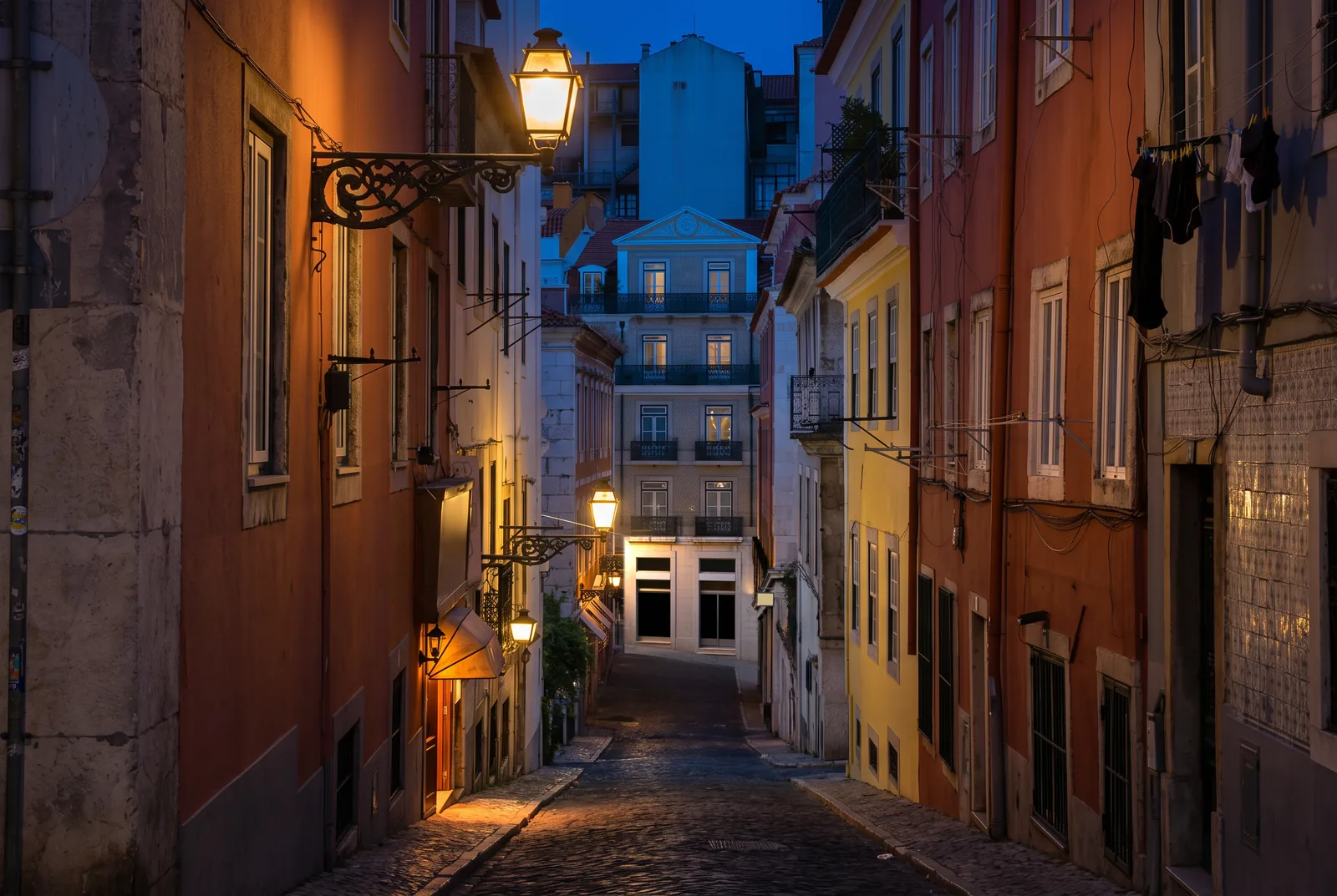 A narrow Bairro Alto street at night lit by iron lanterns