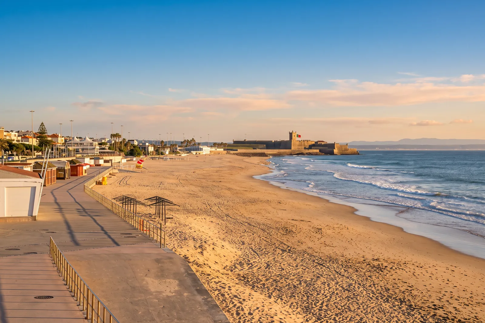 The long sand of Praia de Carcavelos with the promenade and the fort of Sao Juliao da Barra closing the beach
