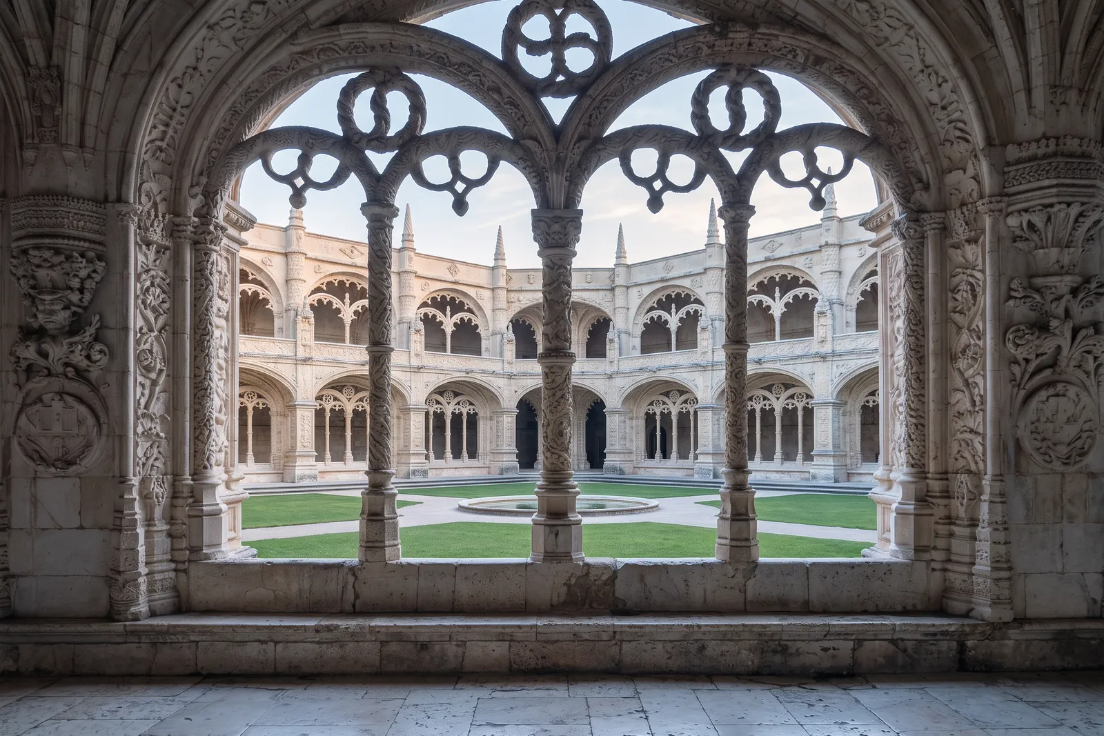 The lower gallery of the Jerónimos cloister, looking through two Manueline arches to the courtyard at first light