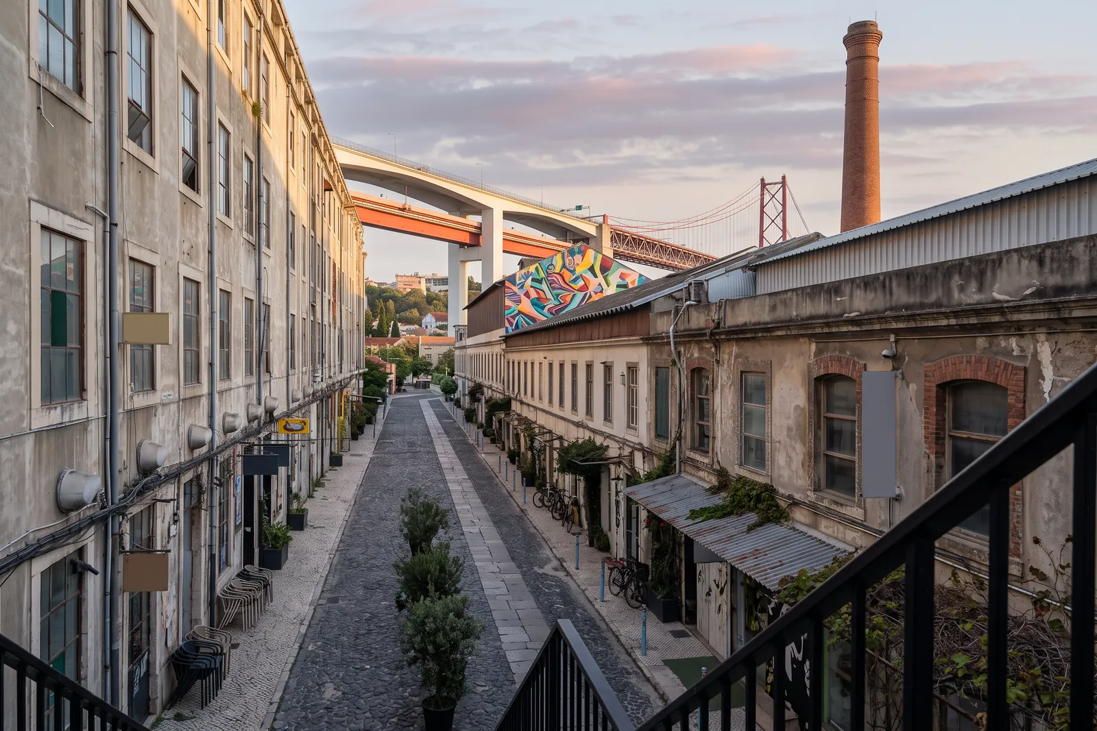 The cobbled main street of LX Factory at sunrise with the 25 de Abril bridge overhead