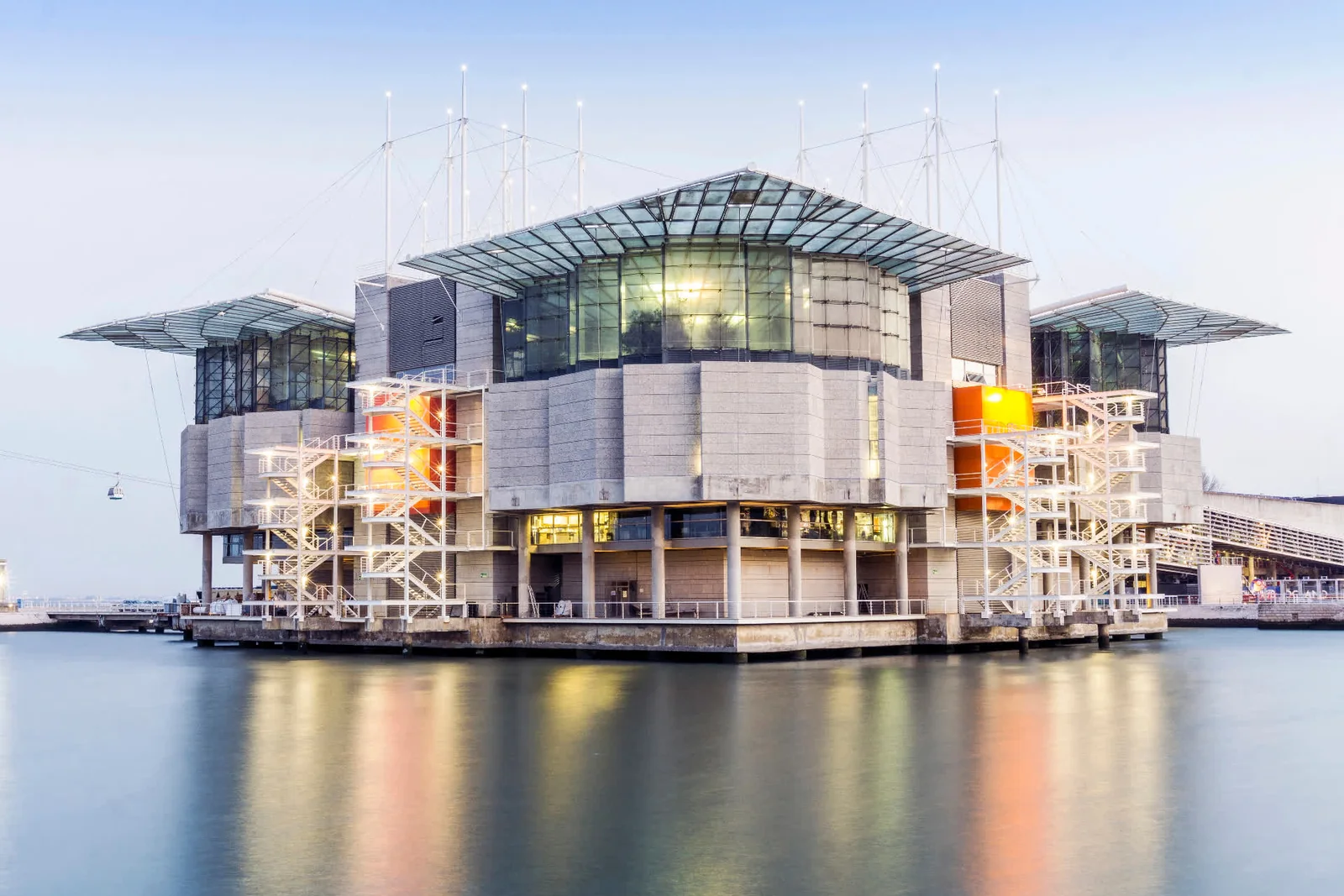 The Oceanário de Lisboa on the water at dusk, its glass roof lit from inside
