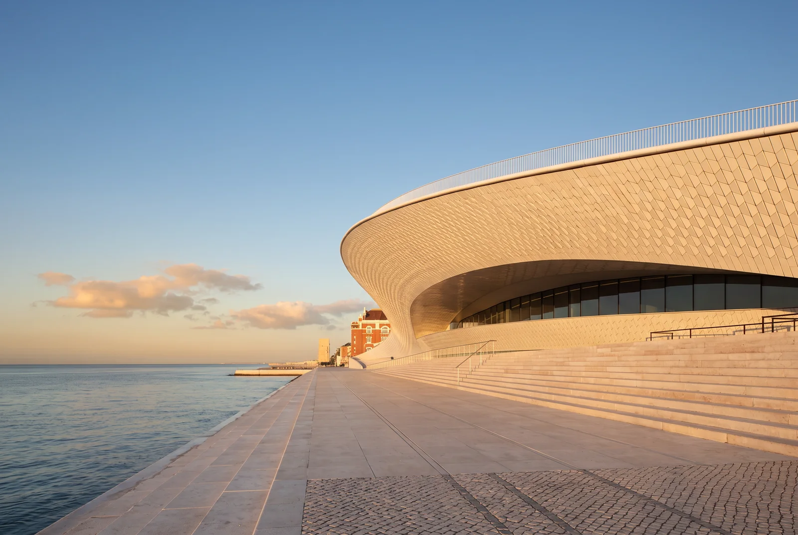 The white tiled roof of MAAT at sunset with the Central Tejo power station and the 25 de Abril bridge beyond