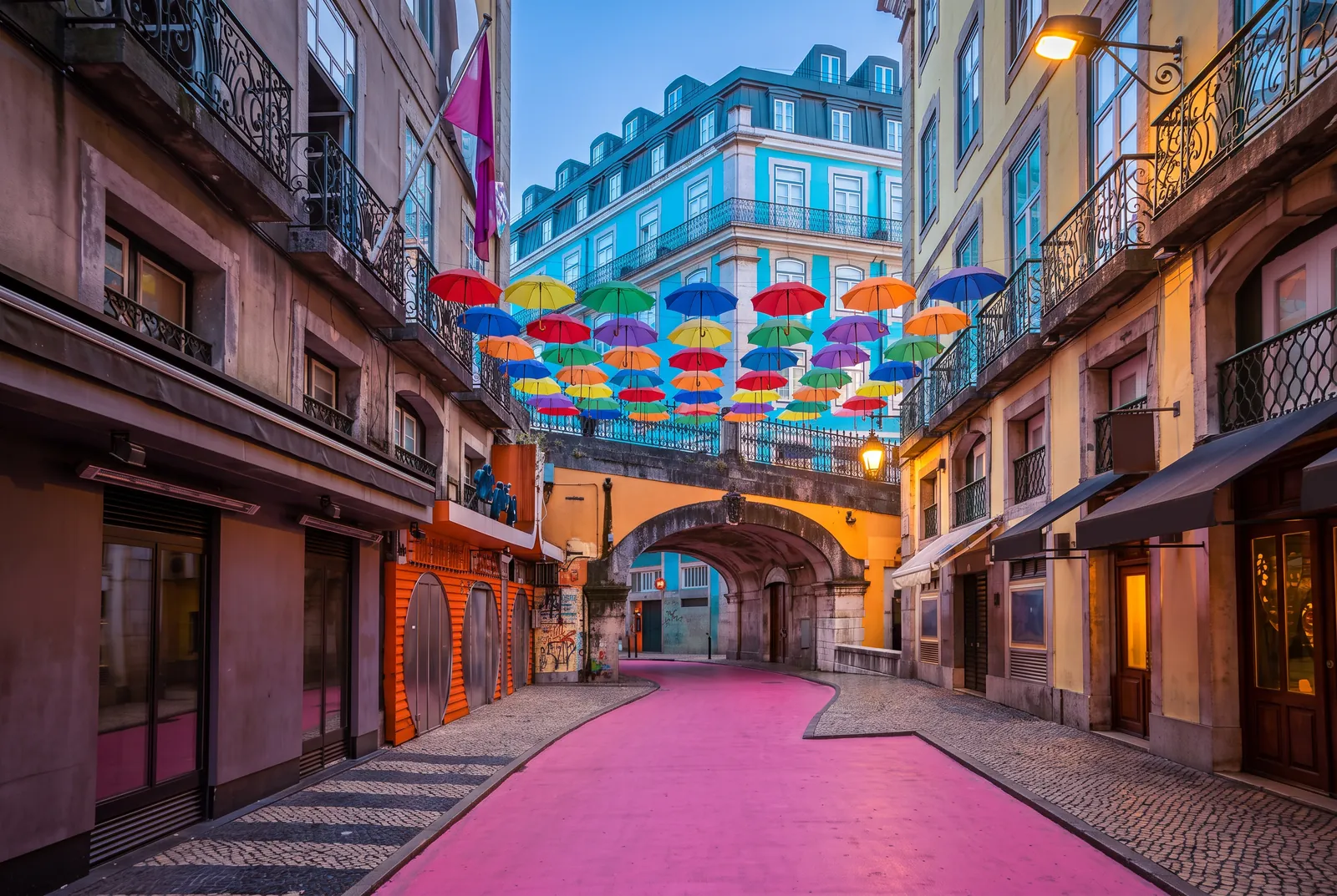 Pink Street seen from under the viaduct arch at dusk, umbrellas strung between the facades