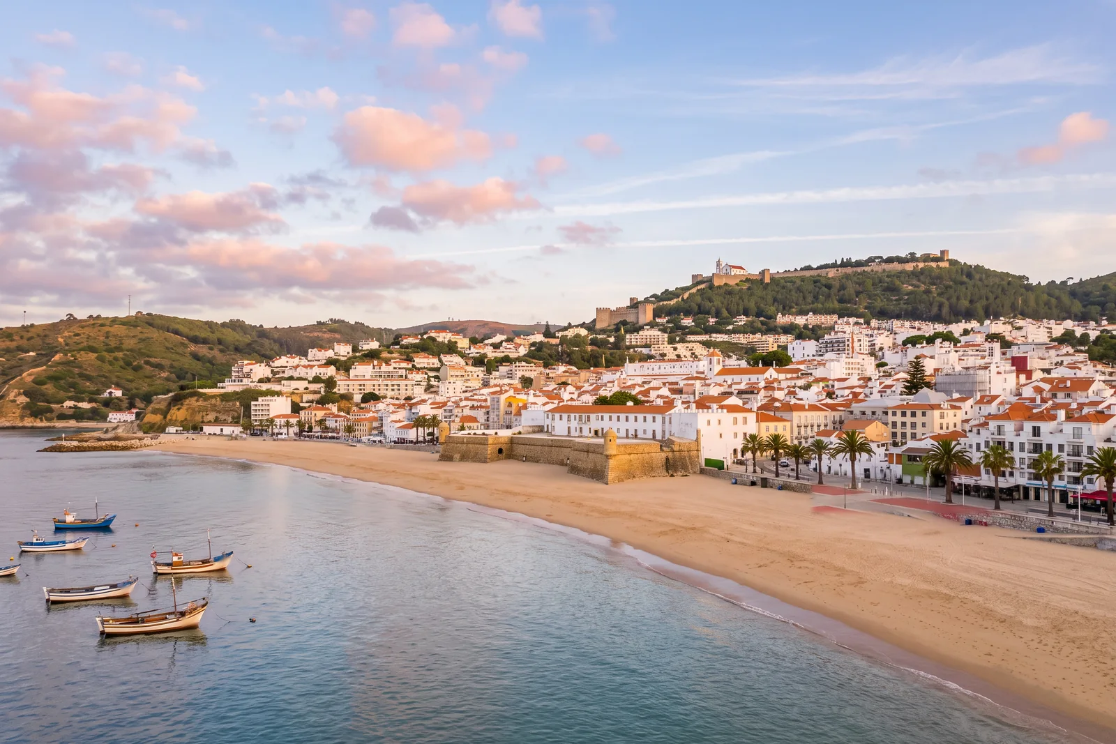 Sesimbra at sunrise from the bay, the Fortaleza de Santiago on the sand between its two beaches, white houses climbing the hill and the castle on the ridge above