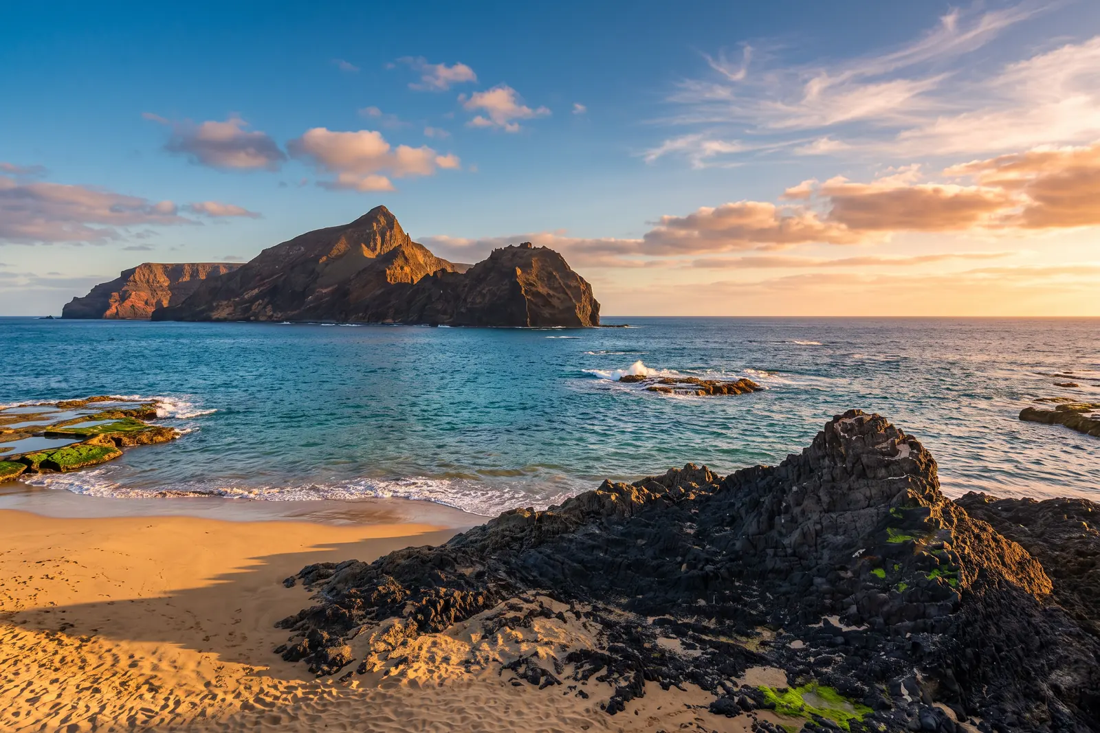 Ponta da Calheta on Porto Santo at golden hour, dark basalt rocks and golden sand facing Ilhéu de Baixo across a turquoise channel