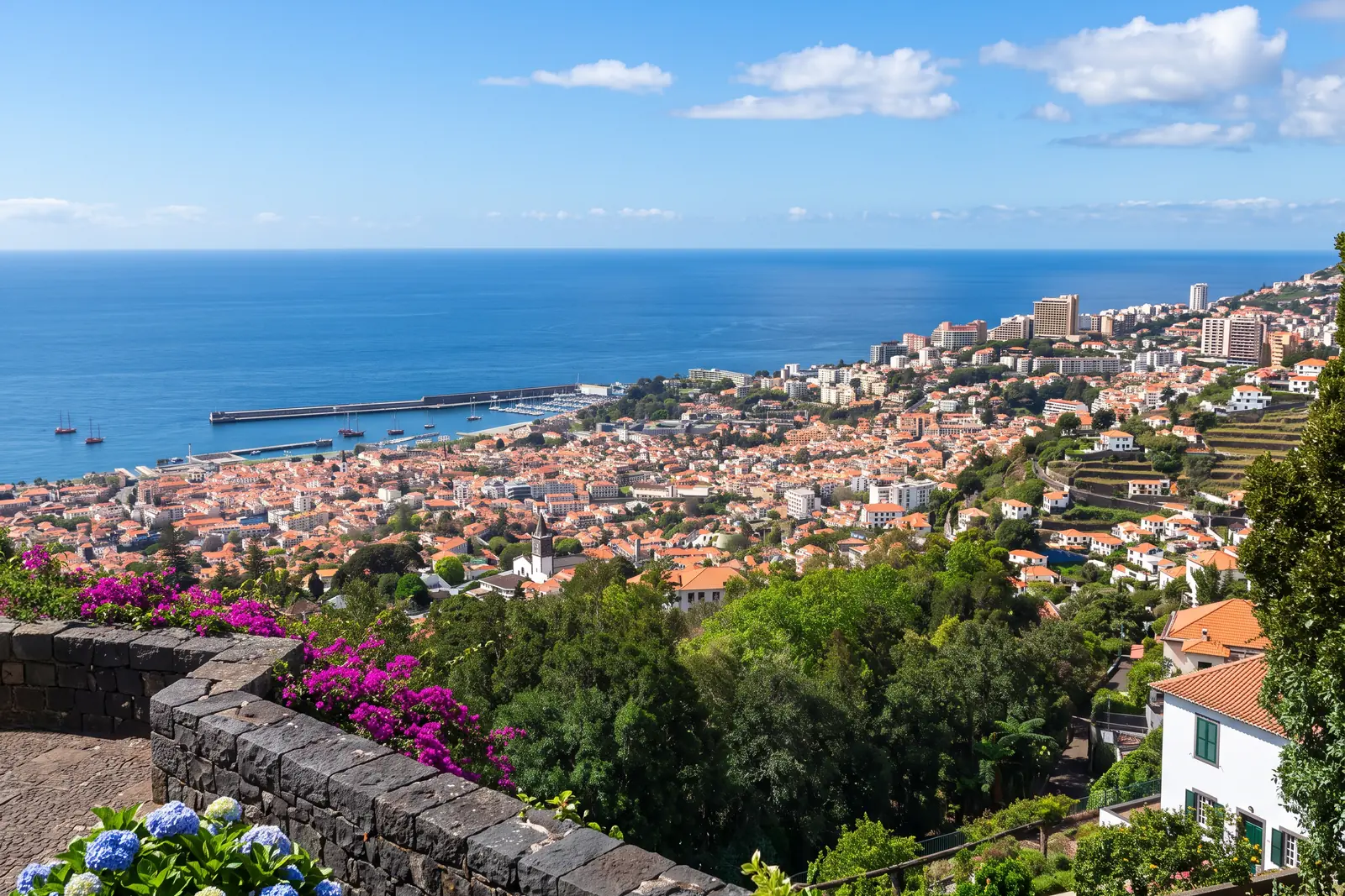 Funchal's terracotta rooftops falling to the harbour and the Atlantic, seen from a stone terrace in Monte