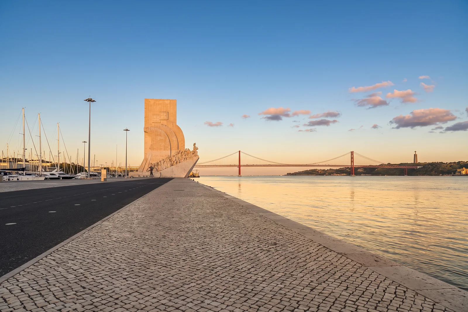 The Belém riverfront at golden hour, with the Monument to the Discoveries, the 25 de Abril Bridge and Cristo Rei across the Tagus